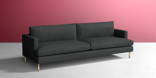 The Bowen 91" Sofa, in a sleek modern dark gray design with two cushions, slim armrests, and elegant gold legs, is showcased against a pink wall and white floor.