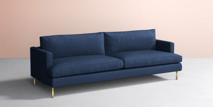 The Bowen 91" Sofa, featuring a modern design with two large seat cushions and backrests, is set against a soft beige background. The sofa comes in dark blue and is complemented by sleek, gold legs for a minimalist look.