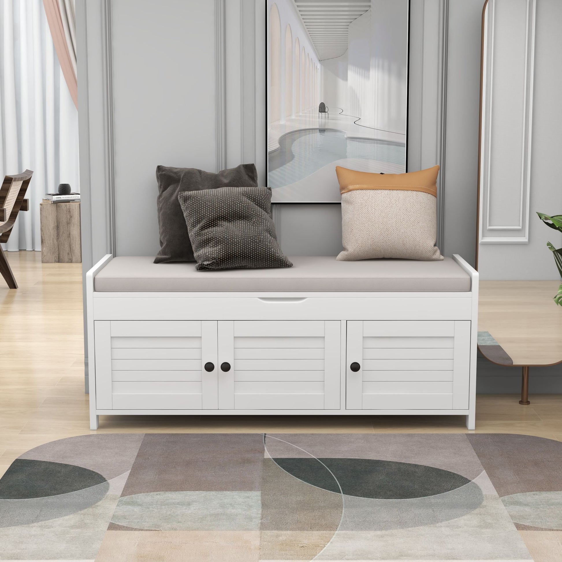 A stylish entryway is highlighted by a storage bench with three shutter-shaped doors, a removable cushioned seat, and hidden storage. On top rest two gray and beige pillows. A neutral-toned rug and modern wall art enhance the contemporary decor.