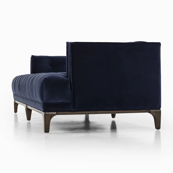 The Dylan Sofa by Four Hands is depicted on a white background, showcasing a modern design with dark blue velvet upholstery, wooden legs, a low back, and sleek rectangular contours with deep cushions.