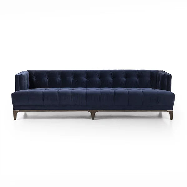 Introducing the Dylan Sofa by Four Hands, a sophisticated and contemporary piece featuring navy blue velvet upholstery with deep button tufting. Its design includes dark wooden legs and a rectangular shape with low back and armrests, all set against a plain white background.