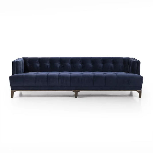 Introducing the Dylan Sofa by Four Hands, a sophisticated and contemporary piece featuring navy blue velvet upholstery with deep button tufting. Its design includes dark wooden legs and a rectangular shape with low back and armrests, all set against a plain white background.