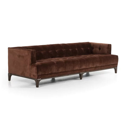 The Dylan Sofa by Four Hands is a luxurious piece featuring a rich brown velvet upholstery with a tufted backrest and sleek dark wood legs. It boasts a modern, elegant design with clean lines, making it ideal for a sophisticated living room setting.