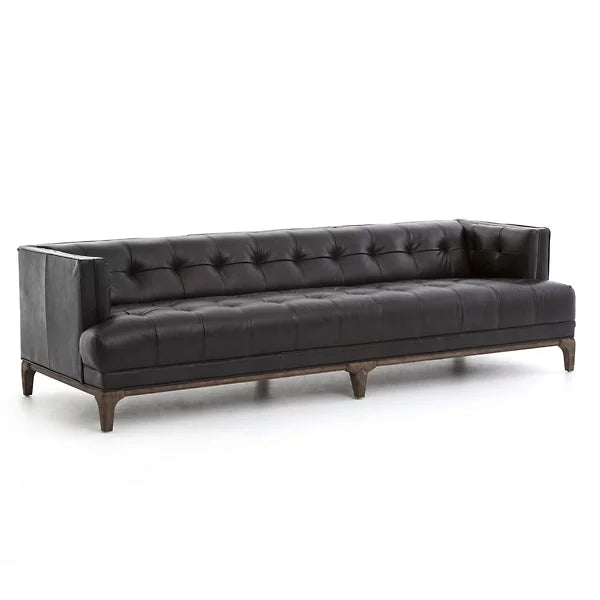 The Dylan Sofa by Four Hands is a contemporary black leather piece featuring a tufted design with deep button detailing and squared armrests. It rests on a wooden base with short legs and is showcased against a plain white background.