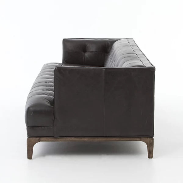 Side view of the Dylan Sofa by Four Hands, featuring a modern, dark brown leather construction with a tufted backrest and seat. The sofa is supported by wooden legs and showcases a sleek, minimalist design set against a plain white background.