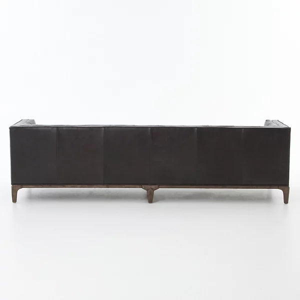 The Dylan Sofa by Four Hands, in dark leather, is showcased from the back to highlight its sleek and modern design with clean lines. It features four tapered wooden legs, all set against a plain white background.