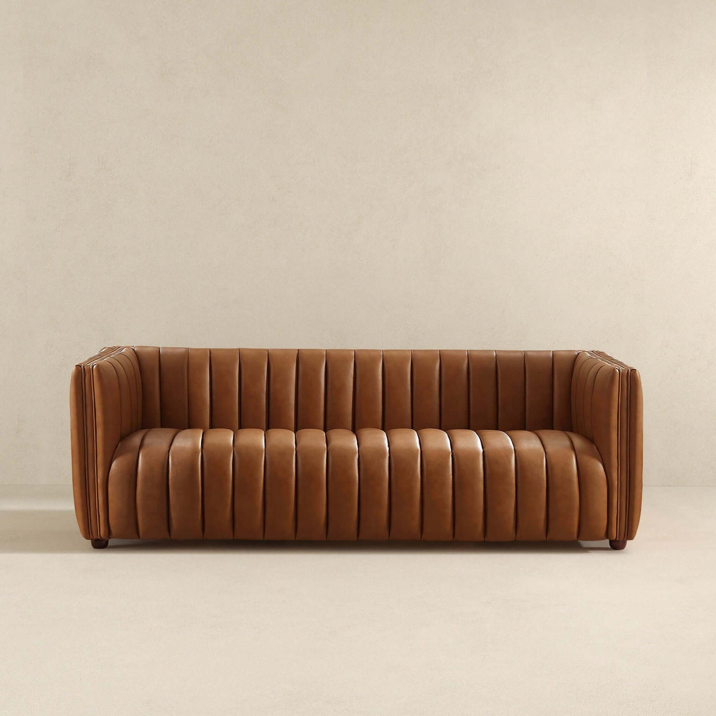 A brown leather three-seater April Mid-Century Modern Luxury Tight Back Boucle Couch with vertical tufted upholstery sits against a beige wall on a light floor, featuring a boxy design, raised armrests, and no visible cushions.