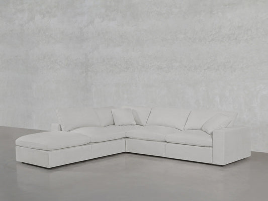 A 5-Seat Modular Corner Lounger Sectional in light gray is elegantly positioned on a smooth concrete floor, set against a textured gray wall. This modern sectional includes plush cushions and features a chaise lounge on the left side, showcasing clean lines.