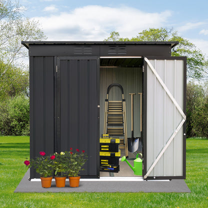 The 4Ftx6Ft Garden Sheds Outdoor Storage Sheds in black metal features open doors revealing a ladder, toolbox, shovel, and green watering can. On the grass outside are three red-flowered potted plants with trees and lawn visible in the background.