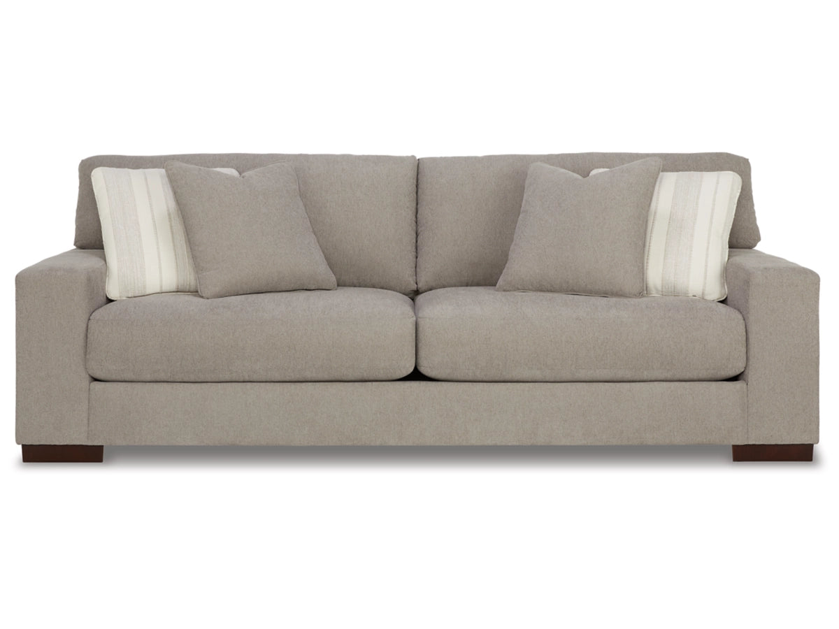 The Maggie Sofa, in light gray, showcases a modern design with sleek lines and wooden feet. It comes with two matching cushions and two striped accent pillows, all set against a plain white background.