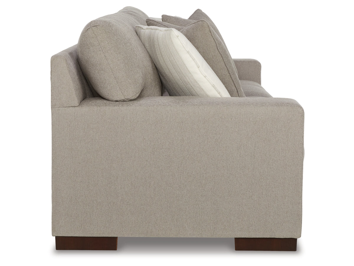 A side view of the Maggie Sofa, crafted in gray fabric with cushioned armrests, and adorned with a variety of pillows in shades of gray and white. The sofa is supported by dark wooden legs.