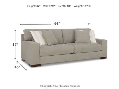 The Maggie Sofa is a beige piece of furniture with dimensions and weight as follows: Height 37 inches, Width 96 inches, Depth 40 inches, Weight 167 lbs. This sofa showcases wide armrests and comes with several cushions, including two that feature striped patterns.