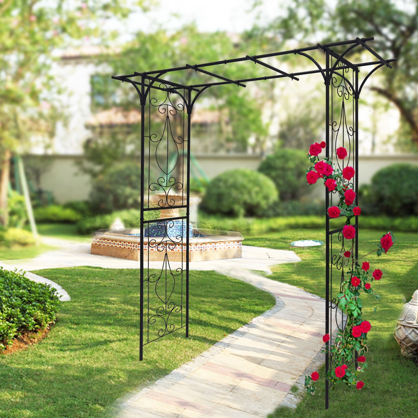 The Metal Garden Arch Climbing Plants Support, a black rose arch, features intricate designs perfect for climbing red roses. It elegantly arches over a curved stone path leading to a circular water fountain surrounded by lush green grass and bushes.