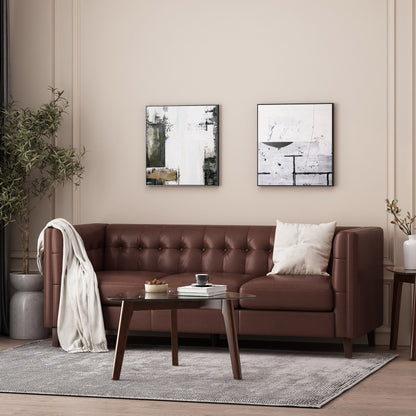 A Comfy 3 Seat Sofa With Tufted Back rests against a beige wall with abstract paintings; it's accessorized with a white pillow and blanket. A wooden coffee table featuring a book, teacup, and candle stands on a gray rug, while a tall potted plant is positioned to the left.