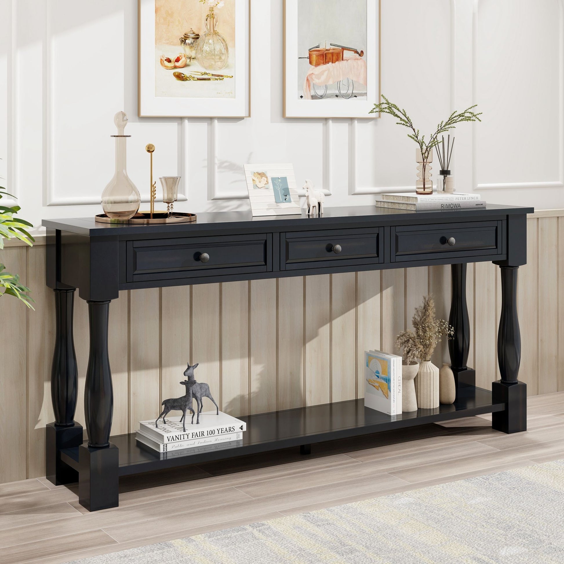 A black Console Table Long Console Table with three drawers stands against a paneled wall, adorned with vases, books, and decor. Framed art pieces hang above it. A small black dog statue sits on the lower shelf.