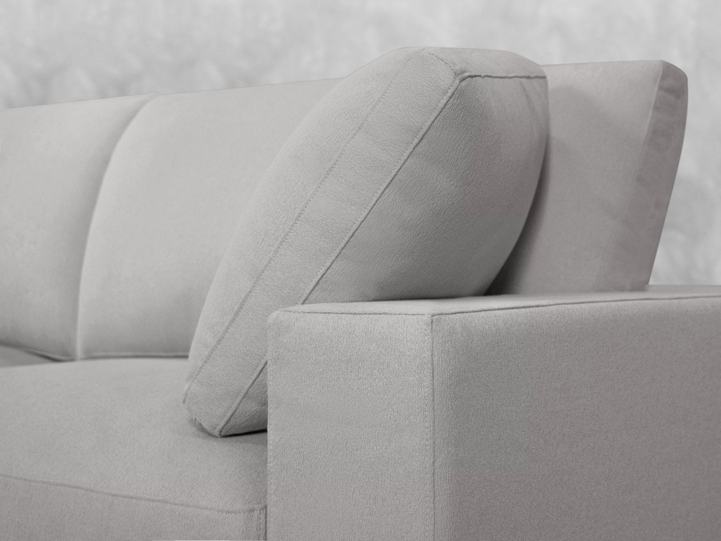 A close-up of the 5-Seat Modular Corner Lounger Sectional in light gray, featuring plush cushions. The focus is on the corner where the cushions meet the armrest, emphasizing the soft fabric texture and clean, modern lines. The background is softly blurred white.