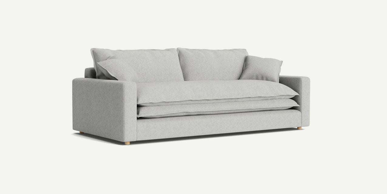 The Meriwether Sofa, featuring a minimalist design, is showcased against a plain background. It boasts plush cushions, wide armrests, and wooden legs in a modern light gray hue.