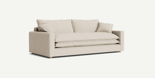 The Meriwether Sofa, featuring a minimalist design in beige with thick cushions, is set against a plain light background. It showcases a straight back, square arms, and two large throw pillows, making it an ideal choice for a contemporary living room.