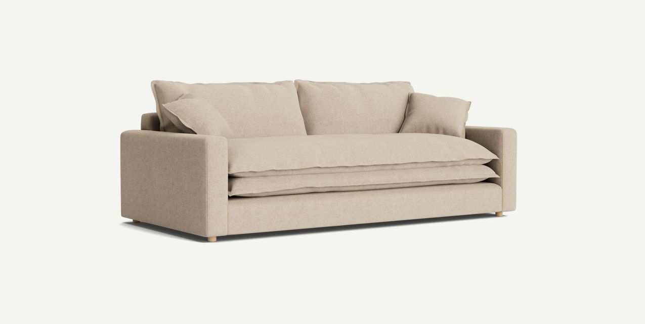 The Meriwether Sofa is a beige, modern piece featuring square armrests and a plush seat, complemented by multiple matching cushions. It stands on short, round wooden legs and is showcased against a plain white background.