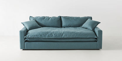 The Meriwether Sofa is displayed against a plain white background and boasts a minimalist, modern design with a plush appearance and deep seat. It features three large cushions on the backrest and two smaller pillows on each side in a stylish teal color.