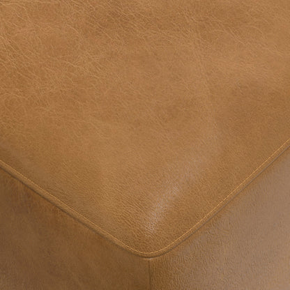 Close-up of a corner of a brown leather sofa or chair, showing the smooth texture and subtle stitching. The surface appears slightly shiny, with visible grain patterns providing a sense of the material's quality.