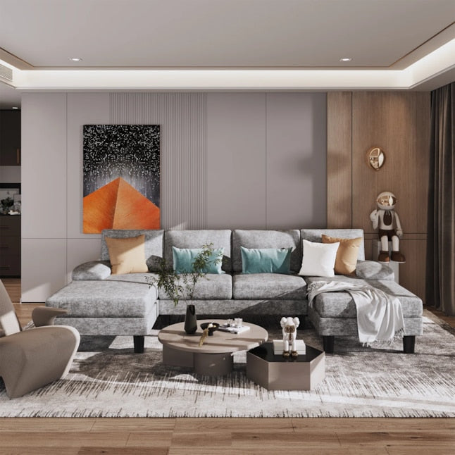 A contemporary living room features the Vineego Modern Gray Chenille Sectional accompanied by colorful cushions and a cozy throw blanket. Abstract artwork adorns the wall while decor and plants are arranged on the coffee table. A decorative figure is placed in the corner, all set against a backdrop of neutral tones.