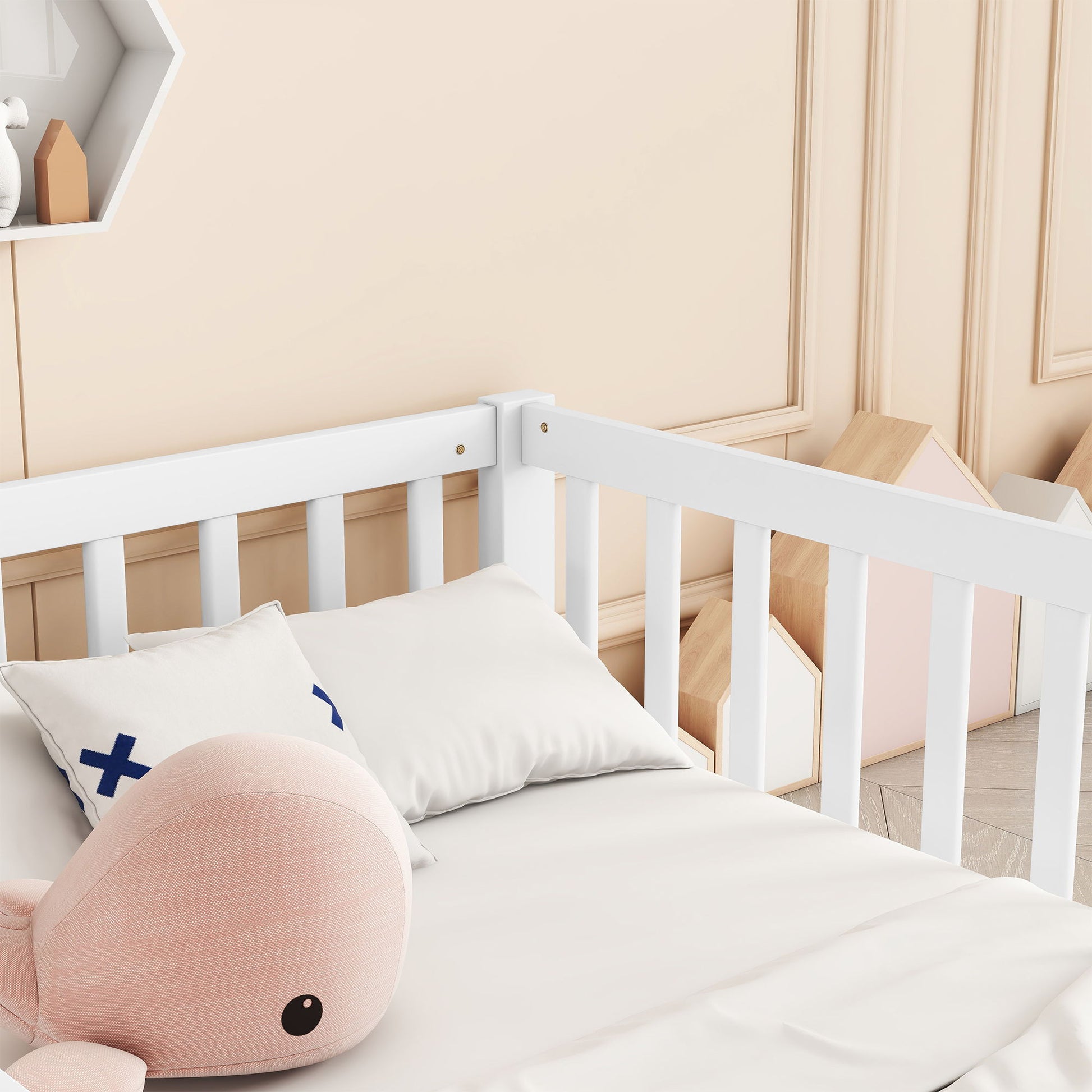 The nursery features a beige wall with decorative panels, a cozy white crib adorned with plush pink whale toy and pillows. In the corner, wooden toy houses stand beside a partially visible hexagonal shelf on the left. The room includes a Double Floor Bed With Fence and Guardrails, No Door.