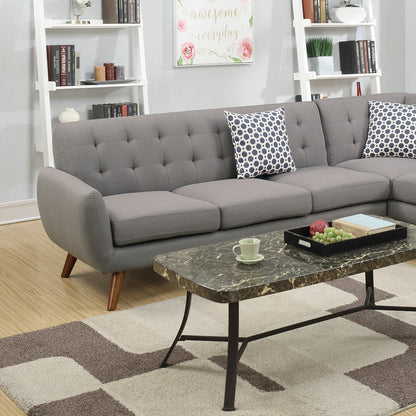 A contemporary living room featuring a Retro Modern Grey Sectional Sofa adorned with patterned pillows. In front, a marble coffee table displays a tray with a green apple and grapes, alongside a cup, while bookshelves and wall art enhance the background decor.