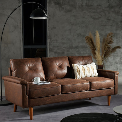 A stylish Ovios 71.65-in Modern Brown Faux Leather 3-seater Sofa, accented with a white cushion and a coffee cup, adds charm to a contemporary living room. A curved floor lamp casts light in the space, while decorative pampas grass stands out against a textured gray wall.