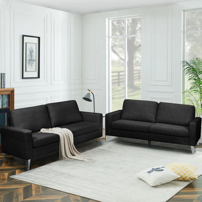 A modern living room featuring two YODOLLA 79" sectional sofas in black, accompanied by a white area rug, a floor lamp, and a couple of cushions placed on the rug. Large windows provide a view of trees and the surrounding field outside. A cozy throw is elegantly draped over one of the sofas.