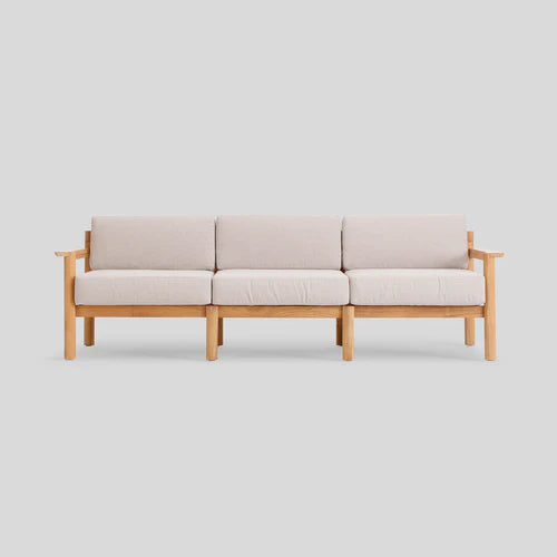 The Haven Sofa, a contemporary three-seater with light-colored cushions and a wooden frame, is showcased against a plain gray background.