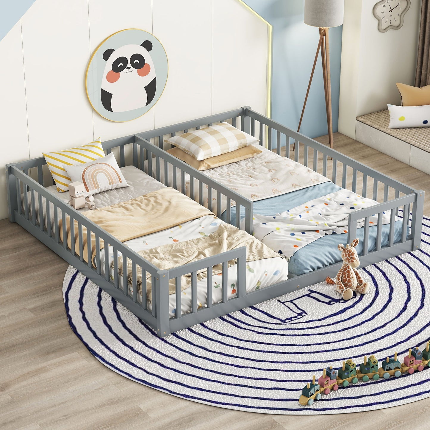 In a children's room, a Double Floor Bed With Fence in gray is adorned with colorful bedding. A panda wall decoration hangs above it. On the floor, there's a round rug with concentric circles, a small giraffe plush toy, and a line of toy blocks nearby.