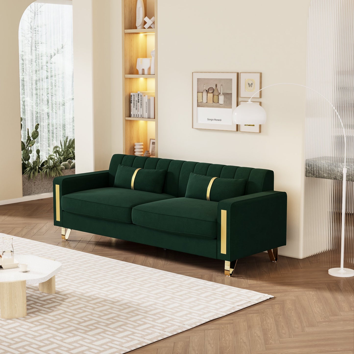 A contemporary living room showcases a Mid Century Modern Sofa Couch in green velvet, highlighted by gold accents and plush cushions. The space features a wooden floor, a geometric-patterned rug, and is illuminated by a floor lamp. Decorative shelves and framed art enhance the beige walls, while greenery can be seen through the windows.