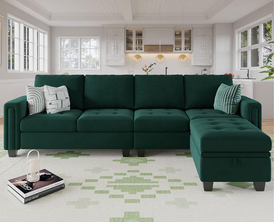 A modern living room features the Belffin Reversible Sectional Convertible Storage sofa, which is green and decorated with striped and geometric pillows. A white and green patterned rug covers the floor, while in the background, you can see a kitchen with white cabinetry and pendant lights.