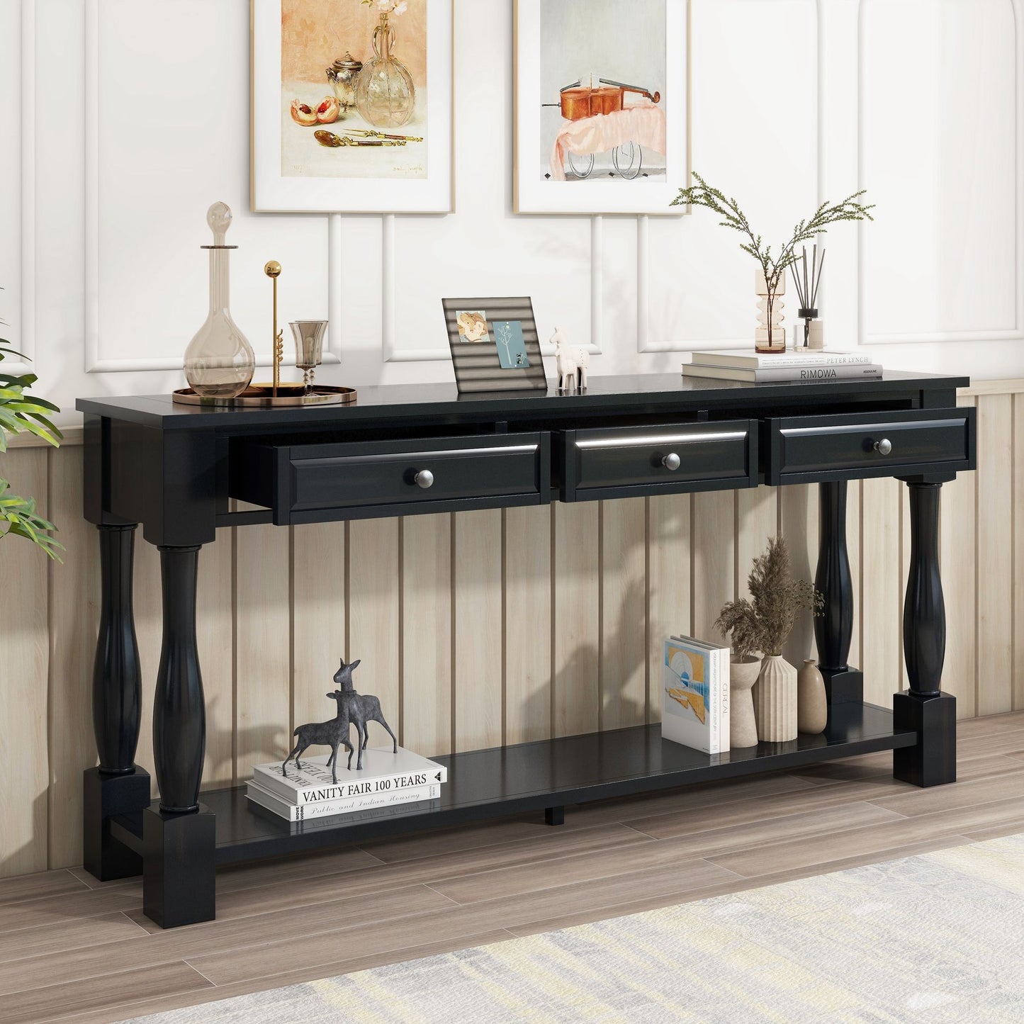 A Console Table Long Console Table with three drawers stands against a paneled wall, showcasing a decanter, framed photos, and books. A magazine and figurine rest on its lower shelf. Artwork is displayed above the table.