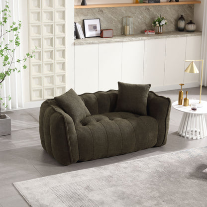 A plush, dark green sofa with two cushions rests on a gray tiled floor alongside a white circular coffee table holding a modern gold lamp. White cabinets and marble backsplash decorate the wall in the background, while greenery is added by a potted plant.