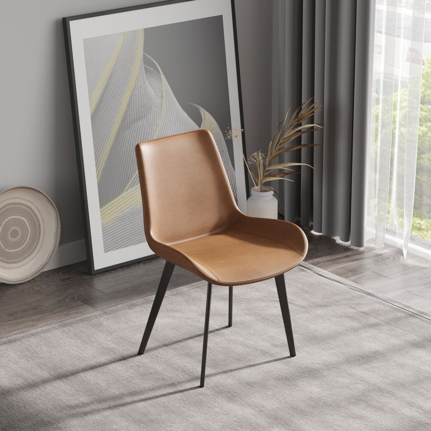 A Modern Dining Chair with brown leather and black metal legs sits on a light gray rug, with an abstract framed artwork behind it. Nearby, a potted plant showcases dried foliage, and gray curtains partially cover a window.