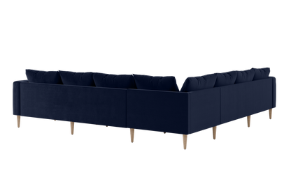 The Essential Corner Sectional (7 Seat) is a spacious L-shaped sofa in deep blue fabric, featuring wooden legs. Its design showcases clean lines and plush cushions, with a view from the back.