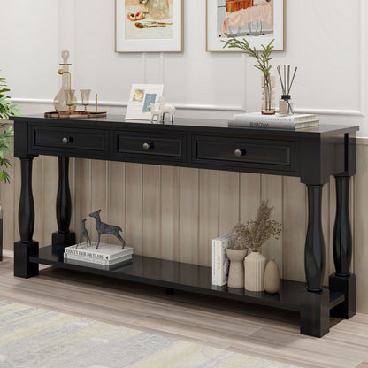 A black console table, featuring three drawers and a shelf, displays small sculptures, books, and a vase. It stands against a light-paneled wall with two framed pictures above it. Part of the floor is covered by a rug.