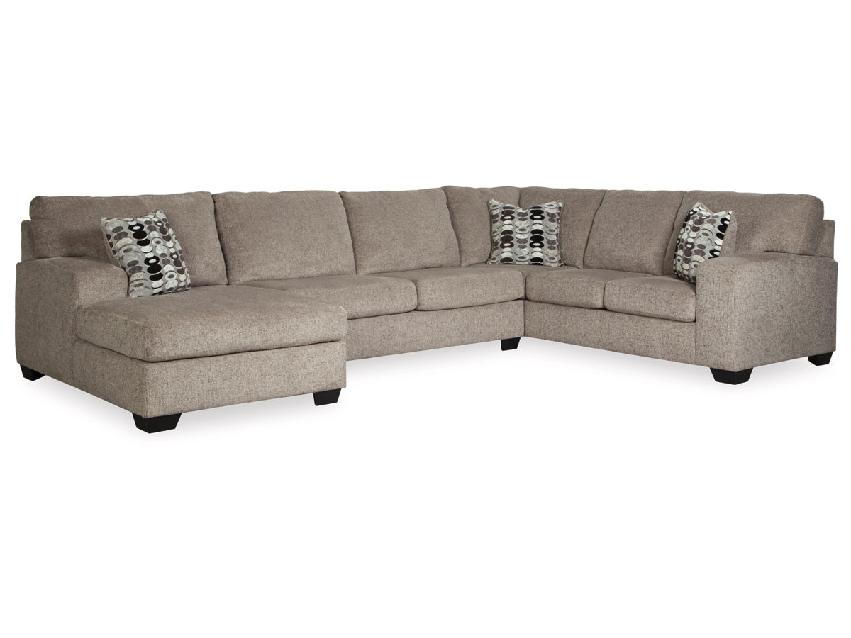 The Ballinasloe 3-Piece Sectional with Chaise is a large, beige sectional sofa featuring a left-side chaise lounge. It stands on dark wooden legs and comes with two patterned throw pillows in black, gray, and white. The sofa is showcased in an L-shape on a white background.