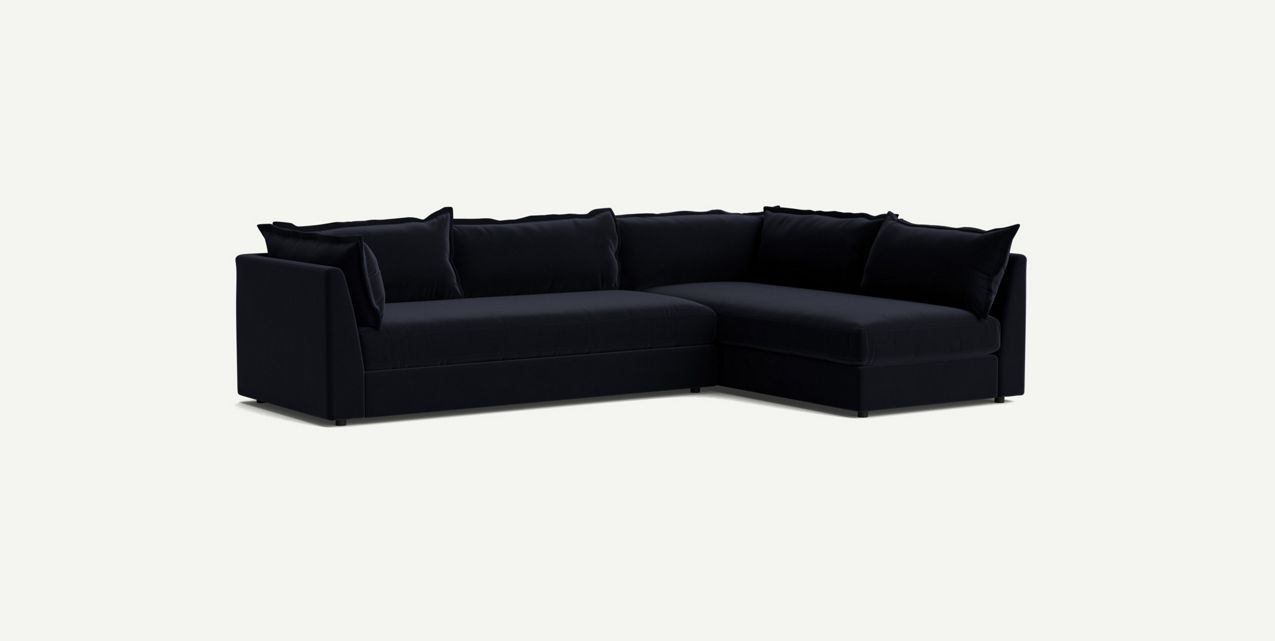 The Denver Two Piece Velvet L Shaped 119" Sectional in black is positioned against a plain white background. With its L-shape design and multiple cushions, the sectional sofa exudes a modern and comfortable vibe, making it ideal for a living room setting.