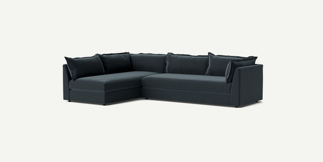 The Denver Two Piece Velvet L Shaped 119" Sectional is a modern dark green sofa with a clean, minimal design. It features plush cushions and a left-facing chaise, set against a plain light background to highlight its sleek and contemporary style.