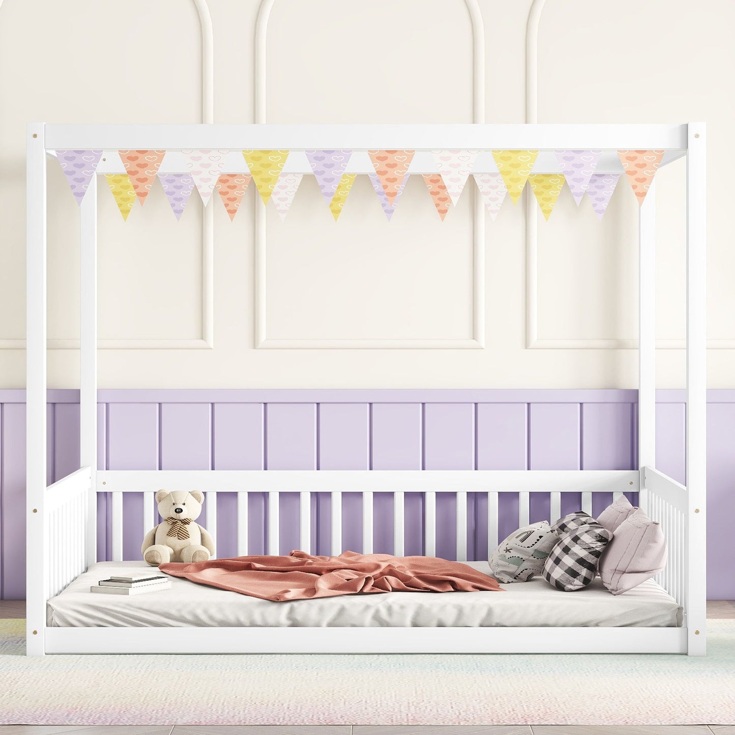 A white Canopy Frame Floor Bed With Fence and guardrails is set against a pastel-paneled wall, featuring a pink blanket, plaid pillows, and a teddy bear. Above the bed hang colorful purple, pink, and yellow triangular flags.