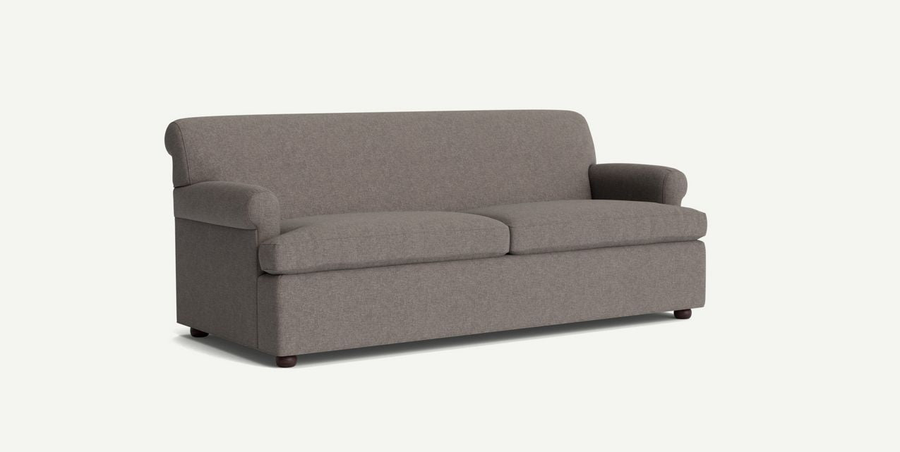 The Willoughby Sleeper Sofa features a simple, modern design with a gray color, rounded armrests, and cushioned backrest and seat. It is presented against a plain light background and showcases its minimalist aesthetic with small wooden legs.