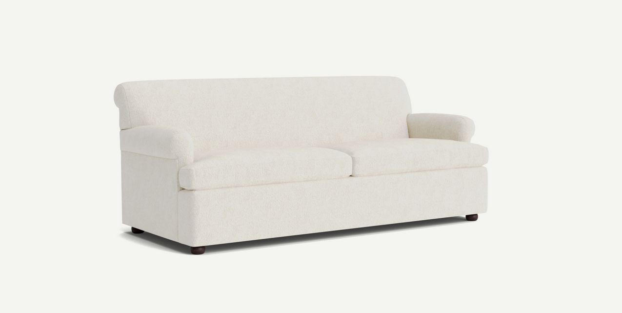 The Willoughby Sleeper Sofa is a beige piece with a simple, modern design. It features two seat cushions and rounded armrests, set against a plain background. The sofa boasts a clean, minimalist appearance with small rounded wooden feet.