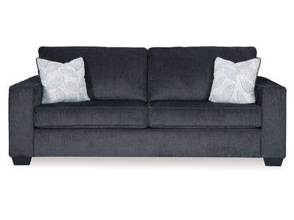 The Altari Queen Sofa Sleeper is a sleek and modern piece in dark gray, featuring two large back cushions and two throw pillows with leaf patterns. It showcases wide armrests and is supported by short, blocky legs for a contemporary look.