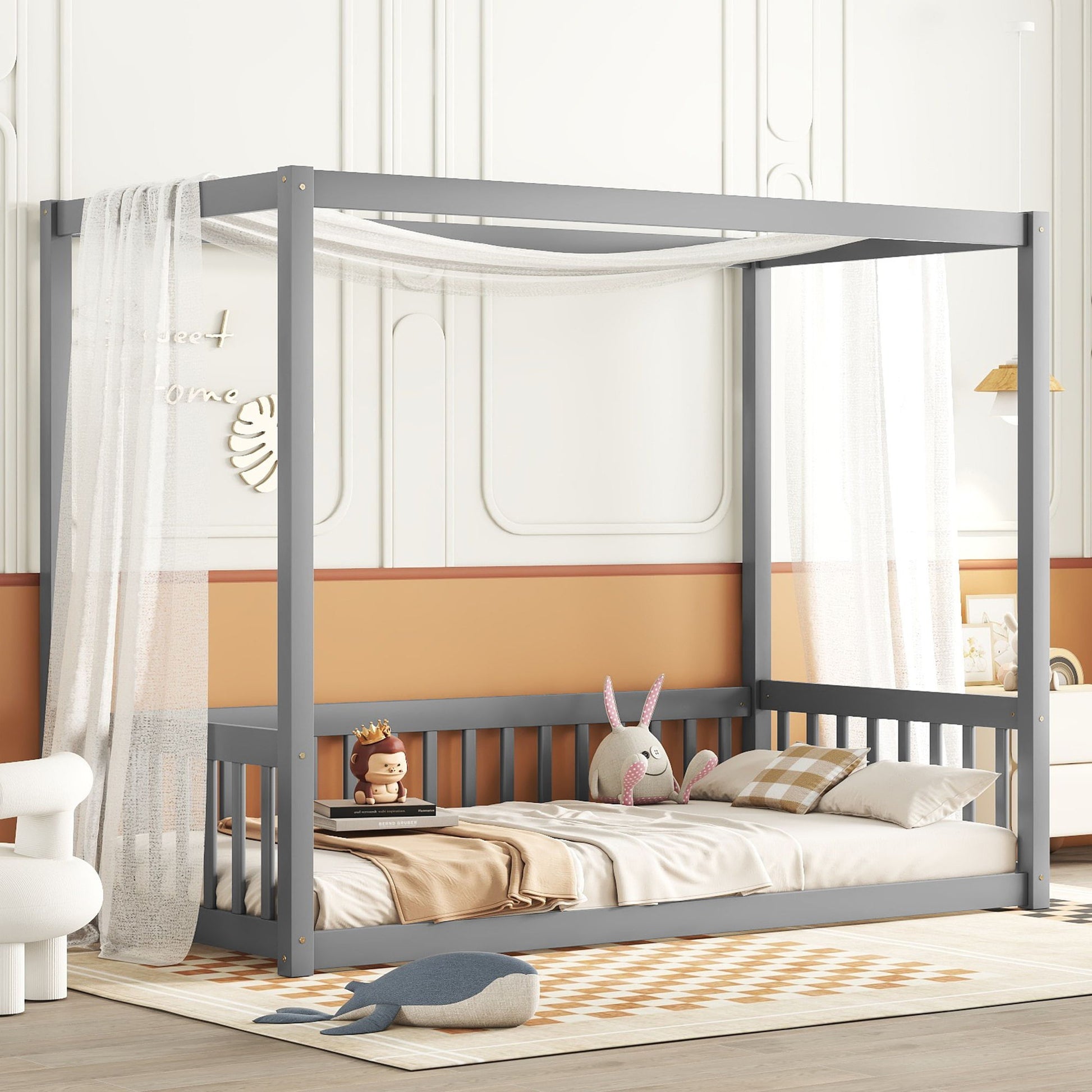 A child's room with a Canopy Frame Floor Bed With Fence, Guardrails, draped in white sheer fabric. The bed has plaid and beige bedding, with stuffed toys including a rabbit and a crown-wearing figure. Soft orange and white colors complement the geometric rug.