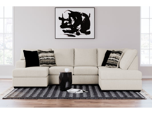 A modern living room featuring the Cambri 2-Piece Sectional with Chaise in cream, adorned with assorted black and striped cushions. Above the sofa hangs a black and white abstract painting. In front, a geometric black coffee table rests on a patterned rug.