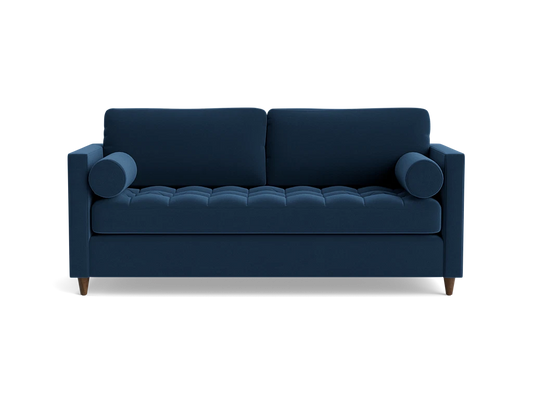 The Briar Sleeper Sofa is a dark blue piece featuring tufted cushions and two round bolster pillows, designed in a modern style with wooden legs that give it a clean, sleek appearance against a black background.