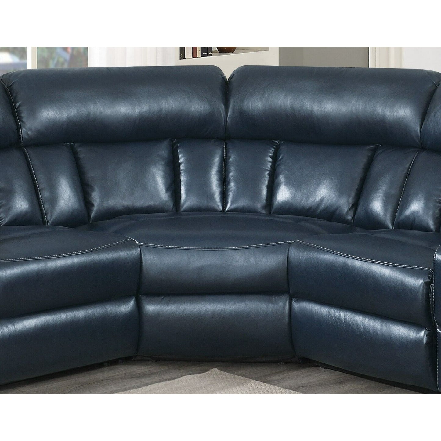 A Luxurious Manual Motion Sectional Sofa in dark blue leather, featuring plush cushions and a curved design, rests on a light-colored floor. The sofa's stitching details are noticeable, with a window and bookshelf partially visible in the background.